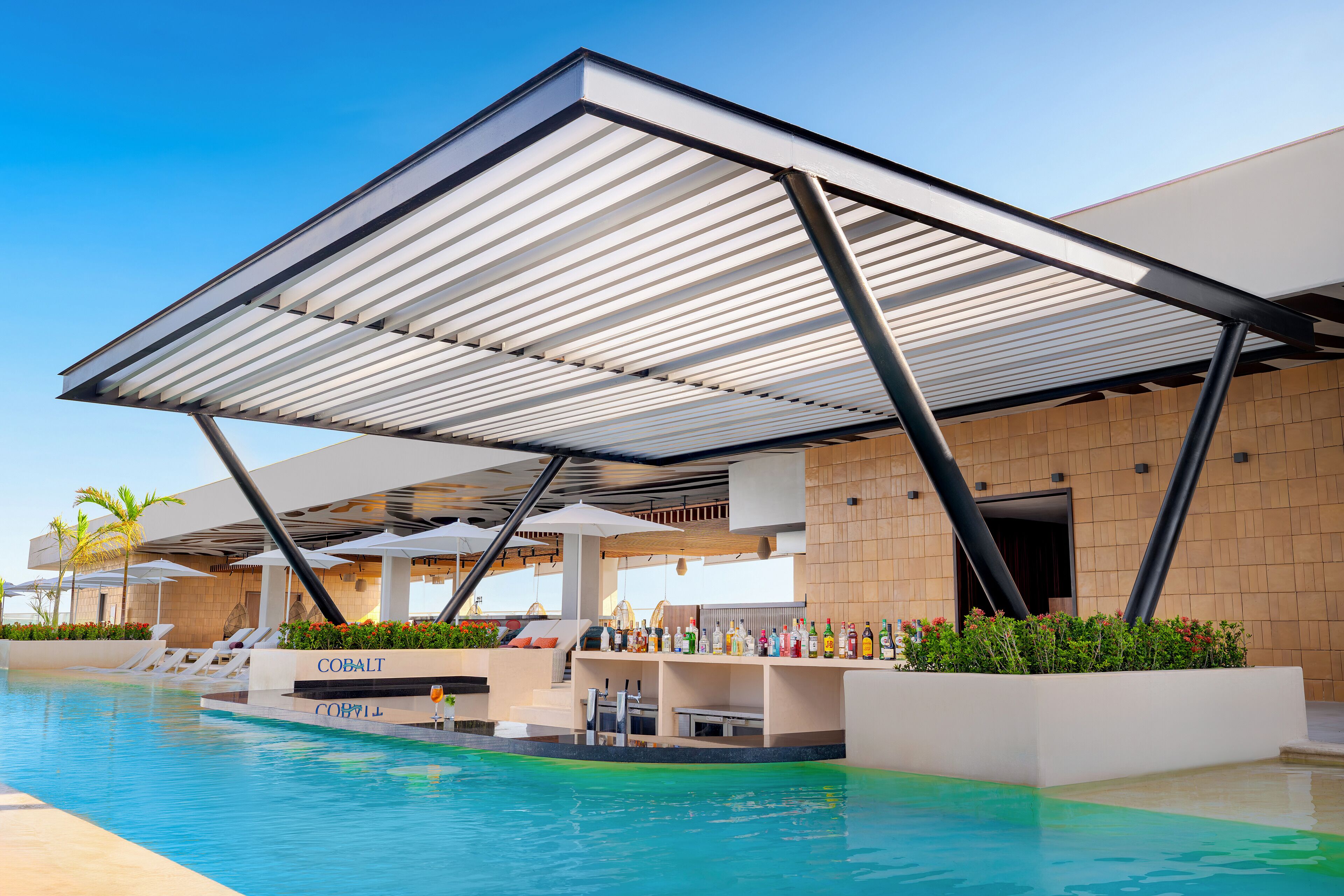 A poolside area with a covered seating area, lounge chairs, and a bar with a variety of bottles.
