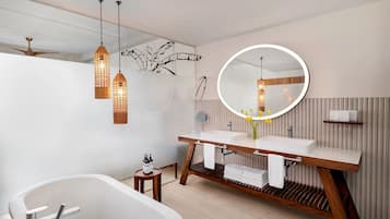 Un baño moderno con una bañera independiente, tocador de madera e iluminación colgante.