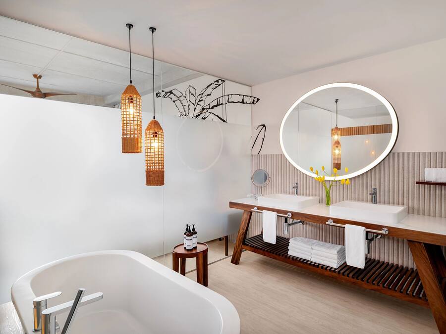 Un baño moderno con una bañera independiente, tocador de madera e iluminación colgante.