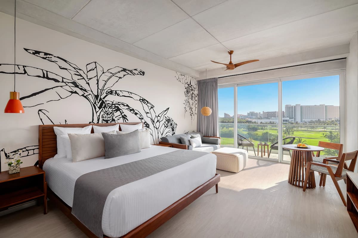 A modern hotel room with a large bed, a balcony with a table and chairs, and a city view.