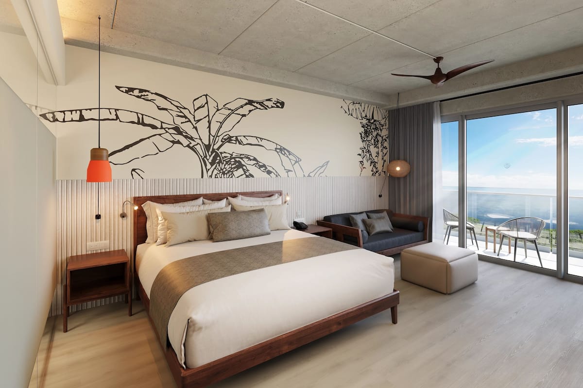 A modern bedroom with a large bed, a sofa, and a balcony with a view.