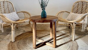 A room with a round wooden table, two wicker chairs, a woven rug, and a mirror on the wall.
