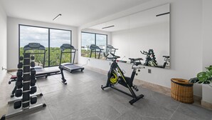 A modern gym with exercise equipment, large windows, and a view of greenery.