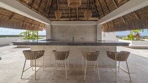 An outdoor bar area with a thatched roof, a stone countertop, and wicker bar stools.