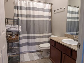 Un bagno con tenda da doccia a righe, un water, un lavabo con piano in granito e uno specchio sopra il lavabo.