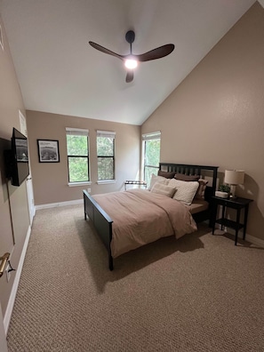 Une chambre à coucher avec un lit, un ventilateur de plafond, une table de chevet, une lampe et deux fenêtres.