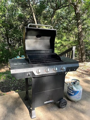 Una parrilla para barbacoa NEXGRILL con cuatro perillas de control, un tanque de gas y una rejilla metálica.