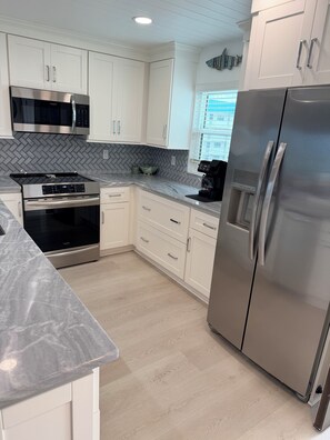 A modern kitchen with white cabinetry, stainless steel appliances, and a herringbone tile backsplash.
