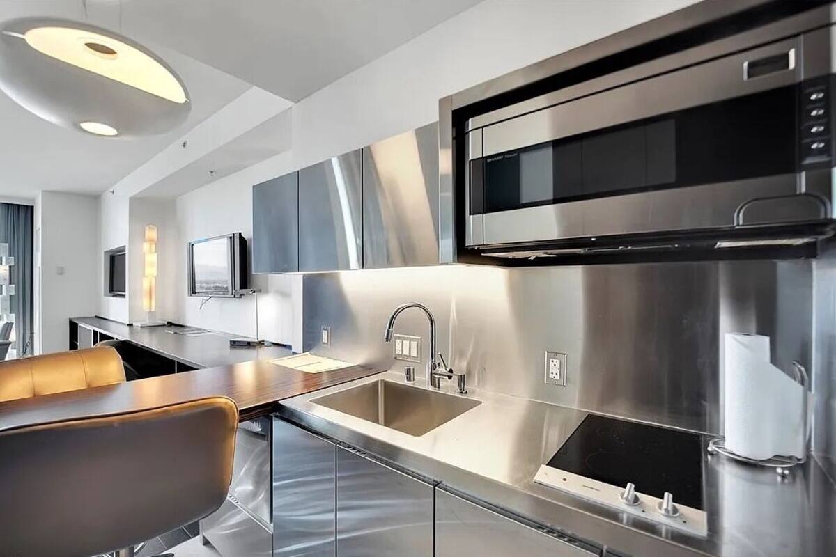 A modern kitchen with stainless steel appliances, a large sink, and a dining area with a table and chairs.