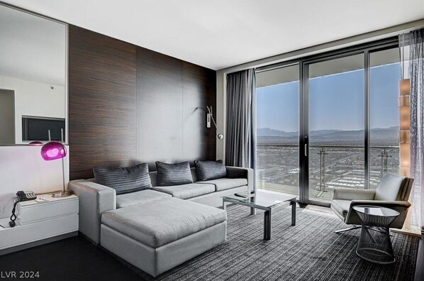 Habitación de hotel moderna con un ventanal amplio que ofrece vistas a la ciudad, un sofá, una silla y una mesita.