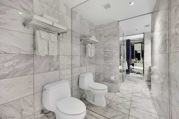 A modern bathroom with marble tiles, two toilets, a glass shower enclosure, and a visible bathroom counter. - Palms Place Condo Hotel & Casino (Las Vegas)