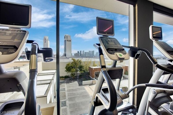 An indoor gym with exercise equipment and a city view through large windows.