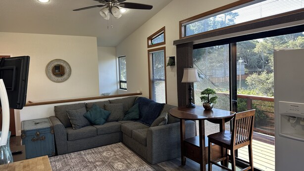 A modern living room with a gray sectional sofa, a wooden coffee table, a small round table with a lamp, and a ceiling fan.
