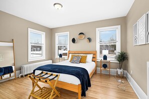 A bedroom with a wooden bed, a window with blinds, a radiator, and a plant.