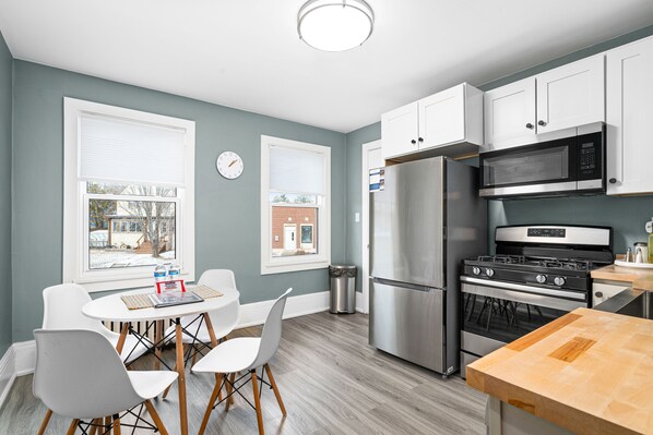 A modern kitchen with white cabinets, stainless steel appliances, and a wooden dining table.