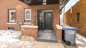 A brick building with a black door, a covered entrance, and a trash bin. - Lakeside Studio | Minutes from Downtown Duluth (Duluth)