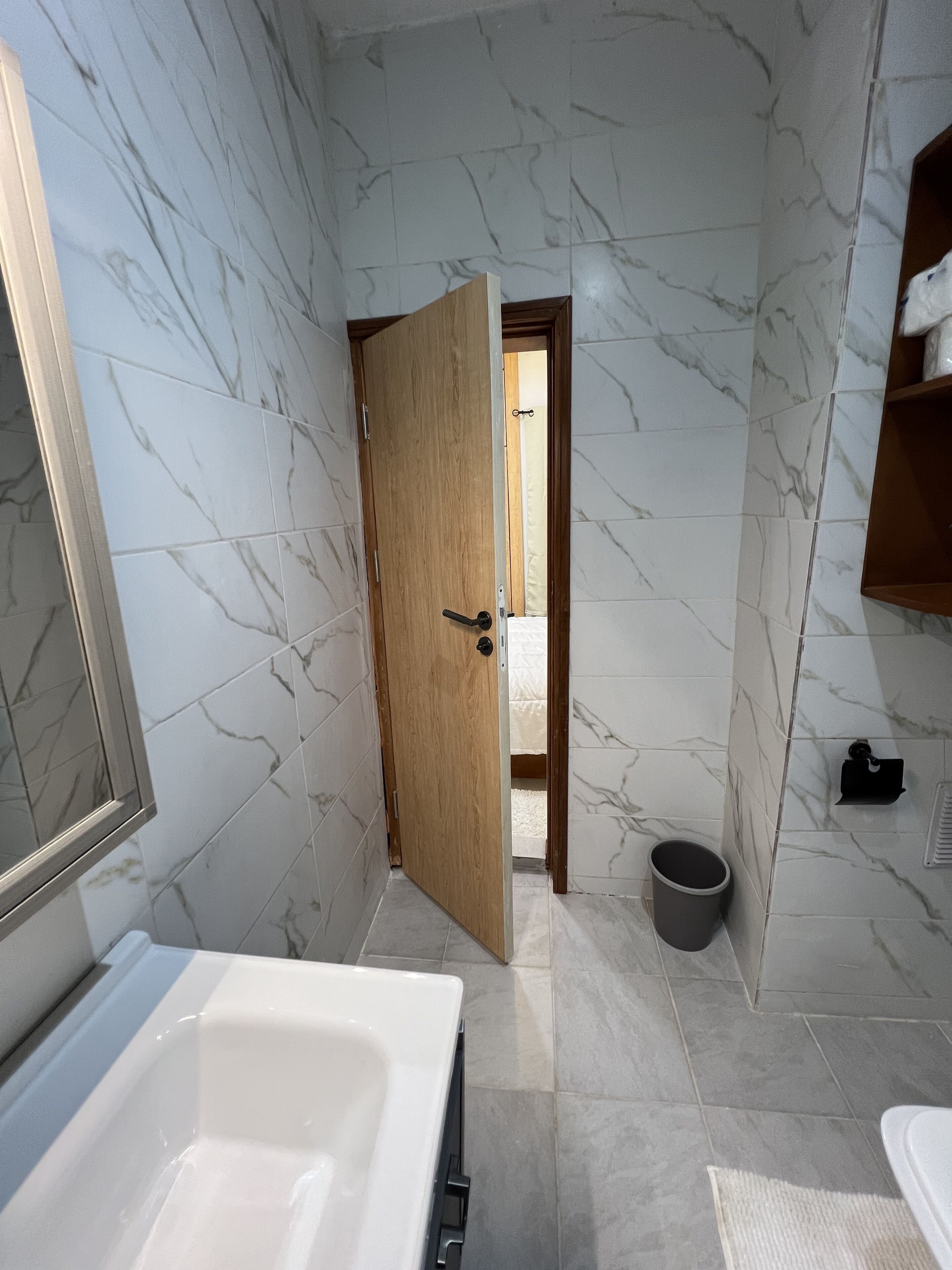 Un baño con pared de mármol, puerta de madera, bañera y retrete.