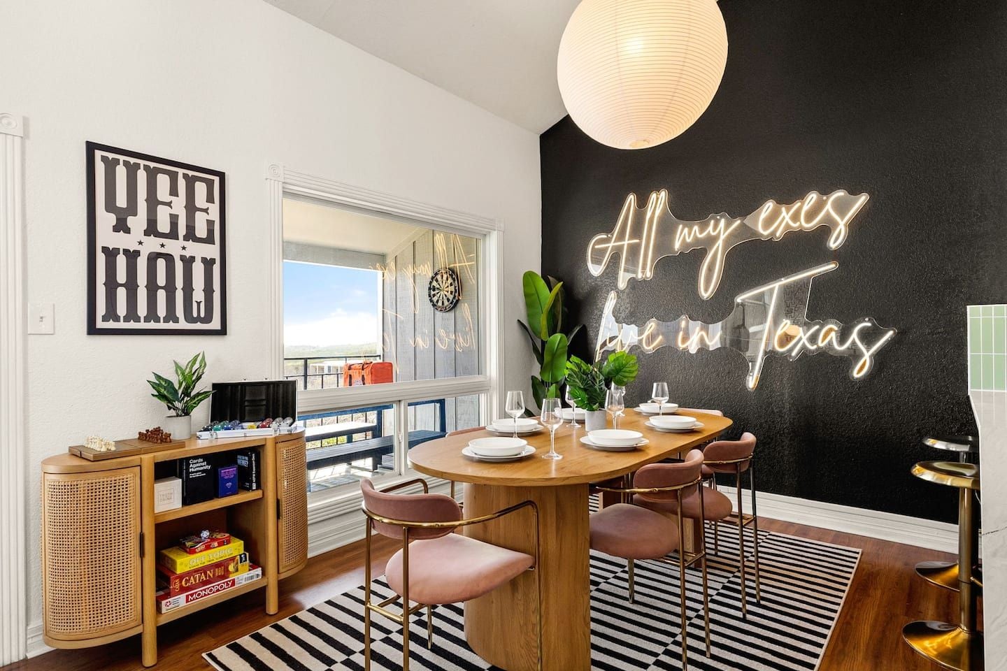 Ein moderner Essbereich mit einem Holztisch, gedeckt für vier Personen, umgeben von Stühlen. Ein Neon-Schild an der Wand zeigt den Text 'All my eyes live in Texas'.