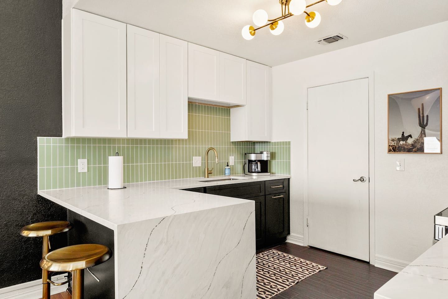 A modern kitchen with white cabinets, a marble island, a coffee maker, and a cactus-themed artwork on the wall.