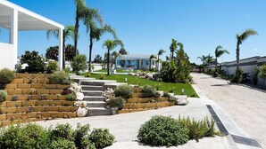 Una casa moderna con un porche cubierto, piscina y un jardín cuidado con palmeras y arbustos.