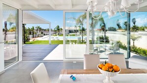 Una habitación moderna con ventanas amplias, una mesa de comedor con fruteros y vista a una piscina y zona exterior.