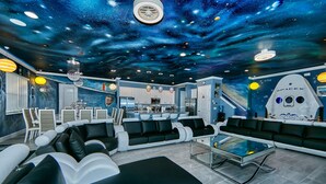 Eine moderne Lounge mit einem himmelsthemenartigen Deckenbild, bequemen Sitzgelegenheiten und einer Küchenzeile im Hintergrund.