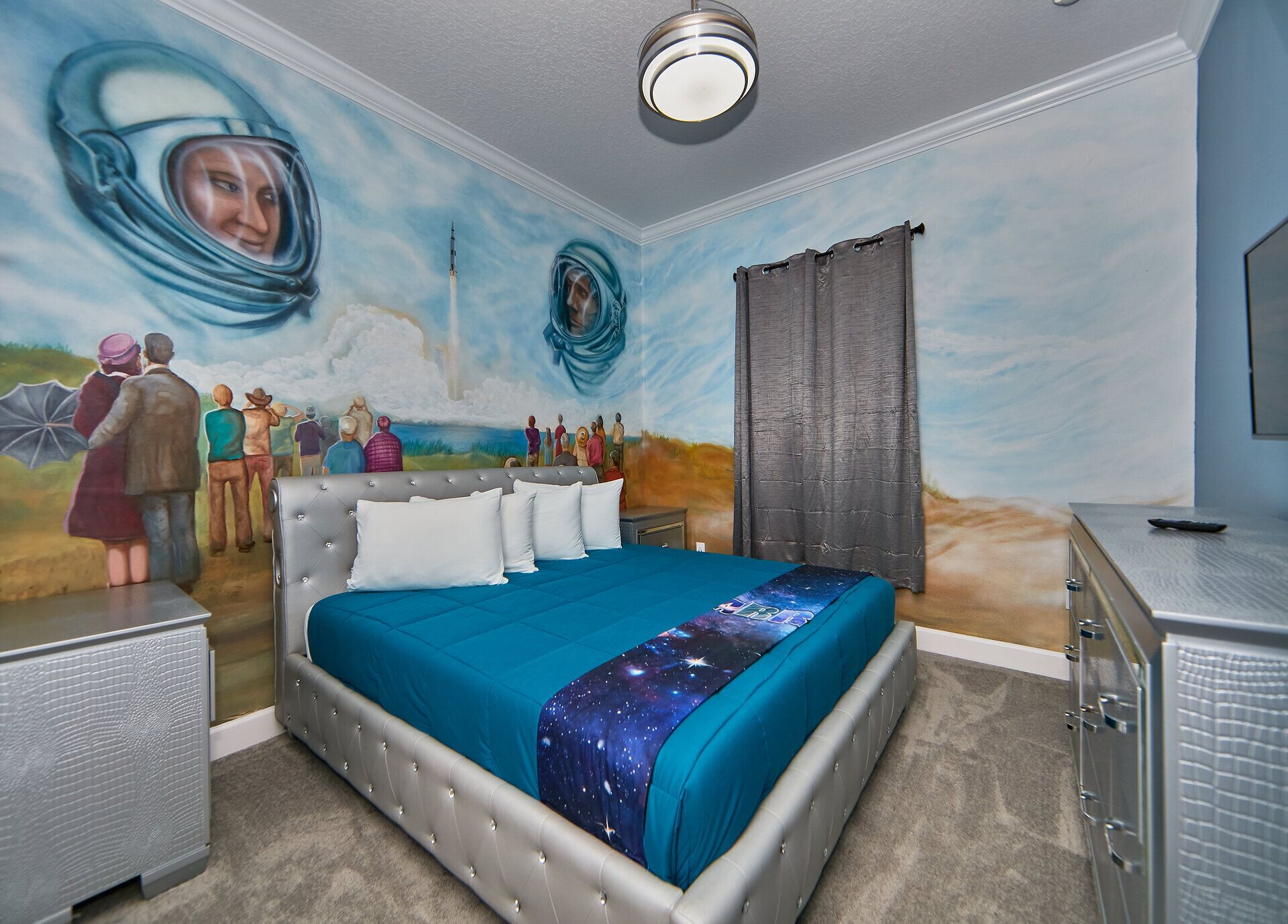 Une chambre à coucher avec une grande fresque murale, un lit à capitonnage, une commode et un luminaire au plafond.