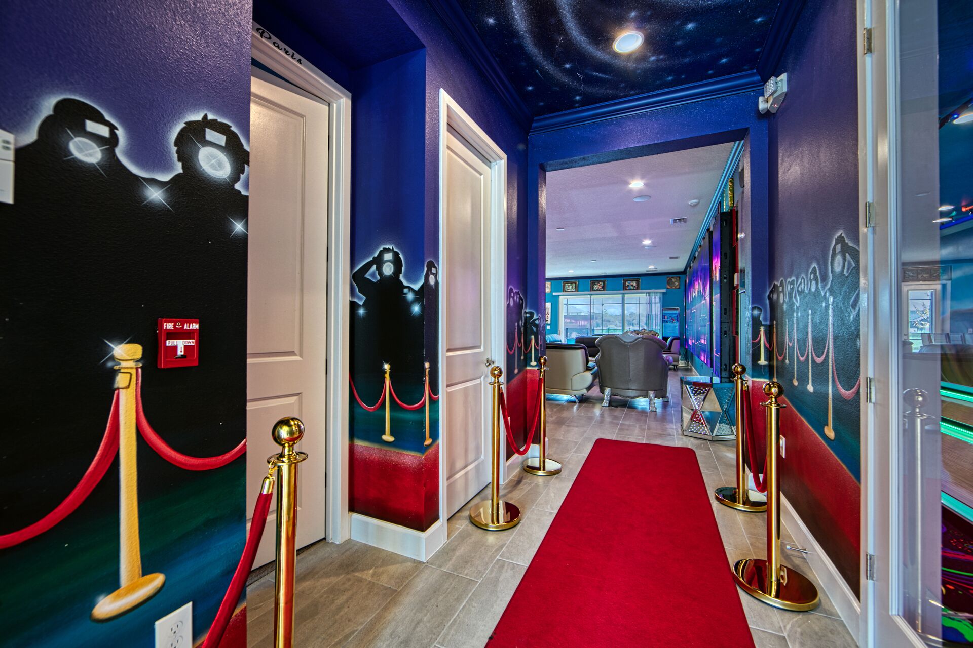 Een hotelgang met een rood tapijt, gouden lintpalen en een sterrenhemelplafond.