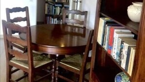 A dining room with a wooden table and chairs, a bookshelf, and a vase on the sideboard.