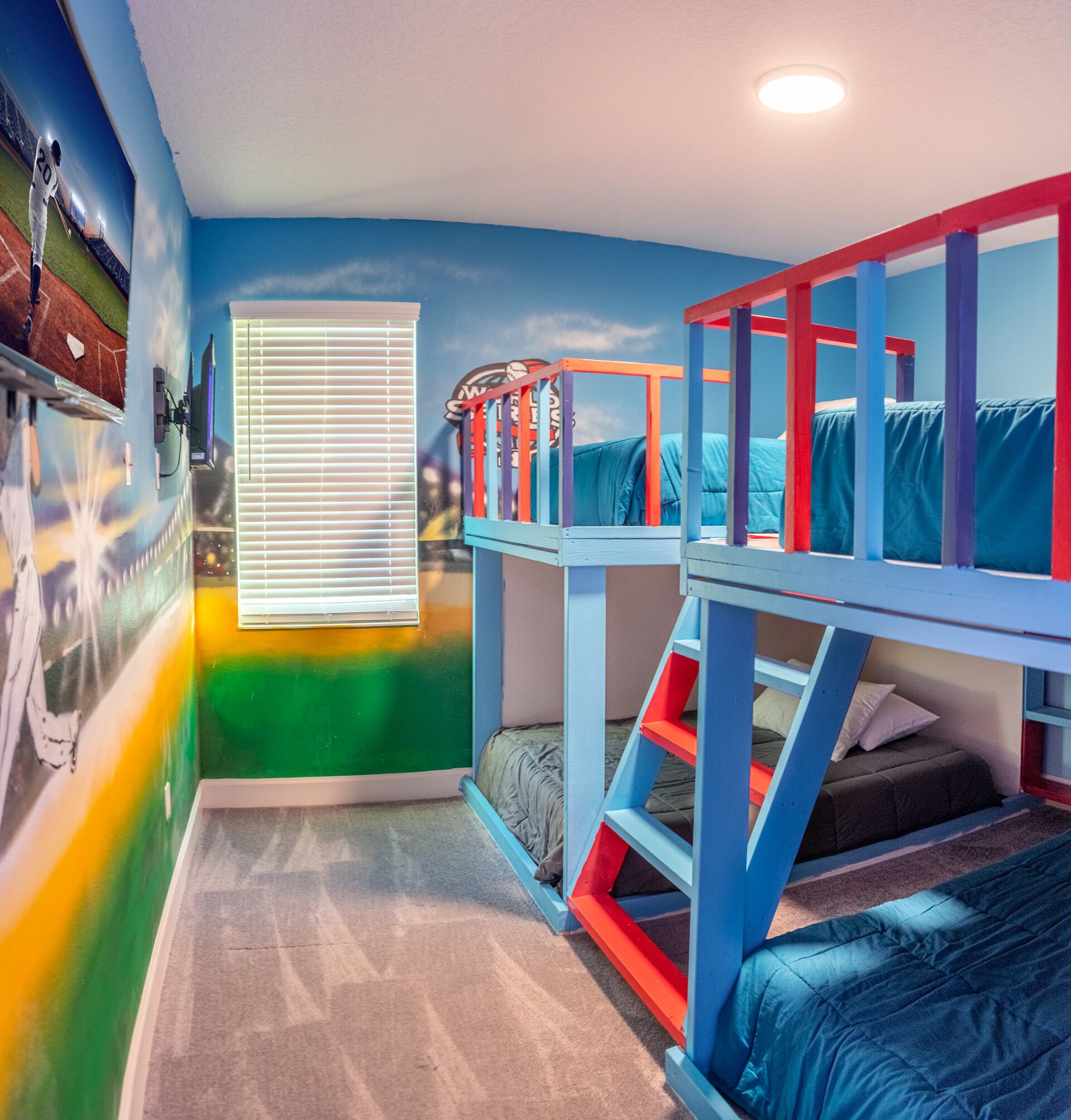 A room with bunk beds, a window with blinds, and a mural on the wall.