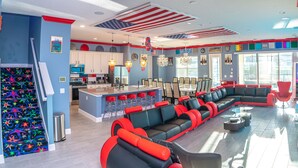 A spacious living area with a large L-shaped sofa, a kitchen with white cabinets, and a bar area with stools.