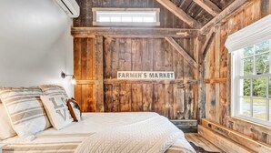 Un dormitorio rústico con cama, almohadas, una colcha, una pared de madera con un letrero, una ventana y una escalera.