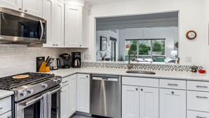A modern kitchen with white cabinetry, stainless steel appliances, a Bosch dishwasher, and a large window offering a view of the outdoors.