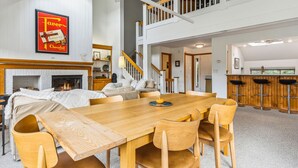 A spacious living room with a fireplace, a dining area with wooden furniture, and a kitchen with bar stools.