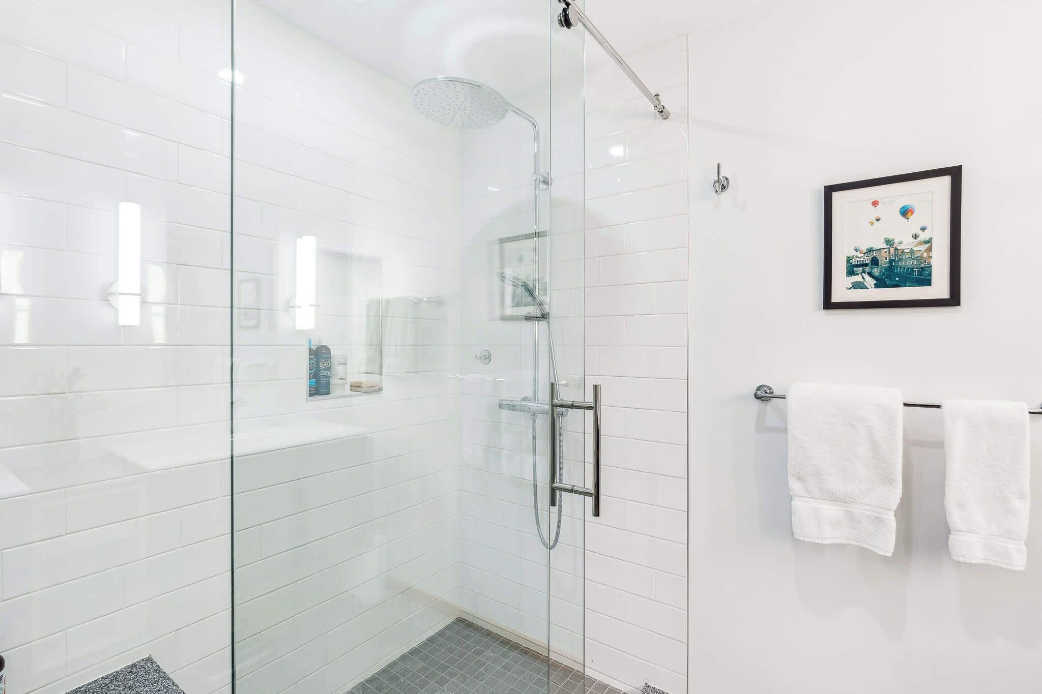 A modern bathroom with a glass-enclosed shower, white tiled walls, and a framed picture on the wall.