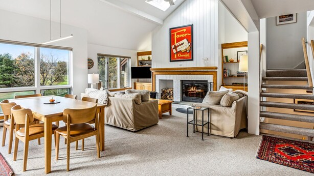 A spacious living room with a fireplace, a dining area, and a staircase leading to an upper level.