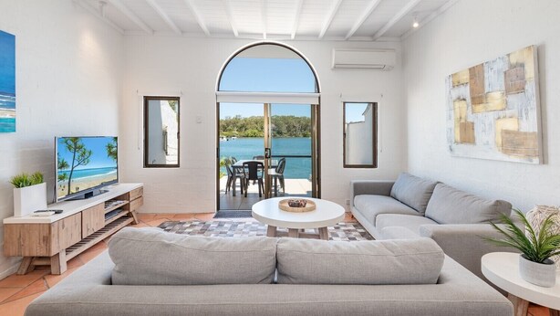 A modern living room with a large window, a flat-screen TV, a sofa, a coffee table, and a dining area with chairs.