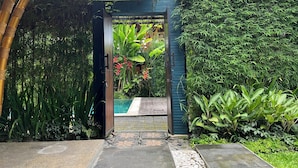 A garden entrance with a wooden gate, a stone pathway, and lush greenery. - Joyously Raw Villas (Ubud)