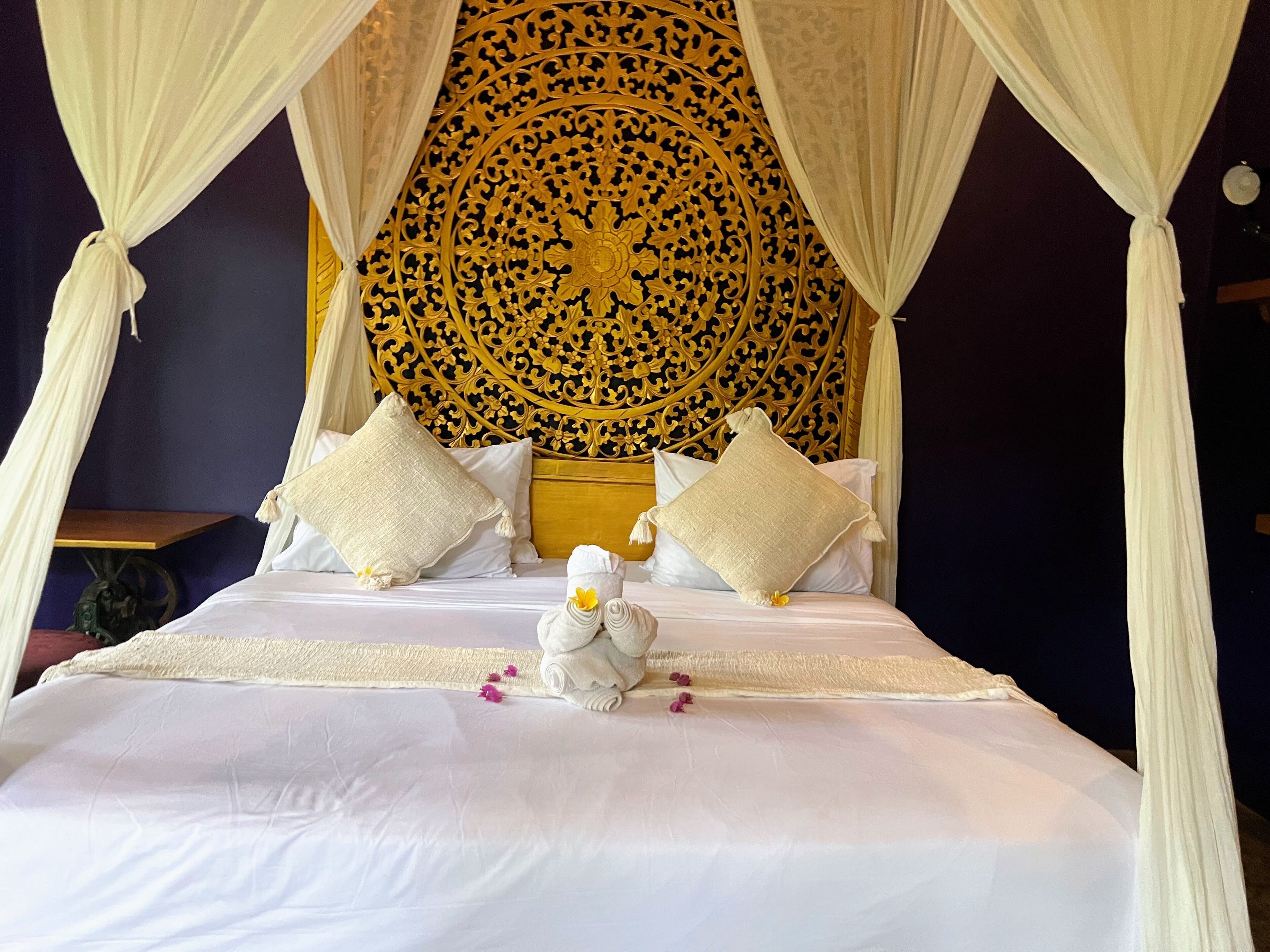 Un letto con baldacchino, cuscini e una testiera decorativa.