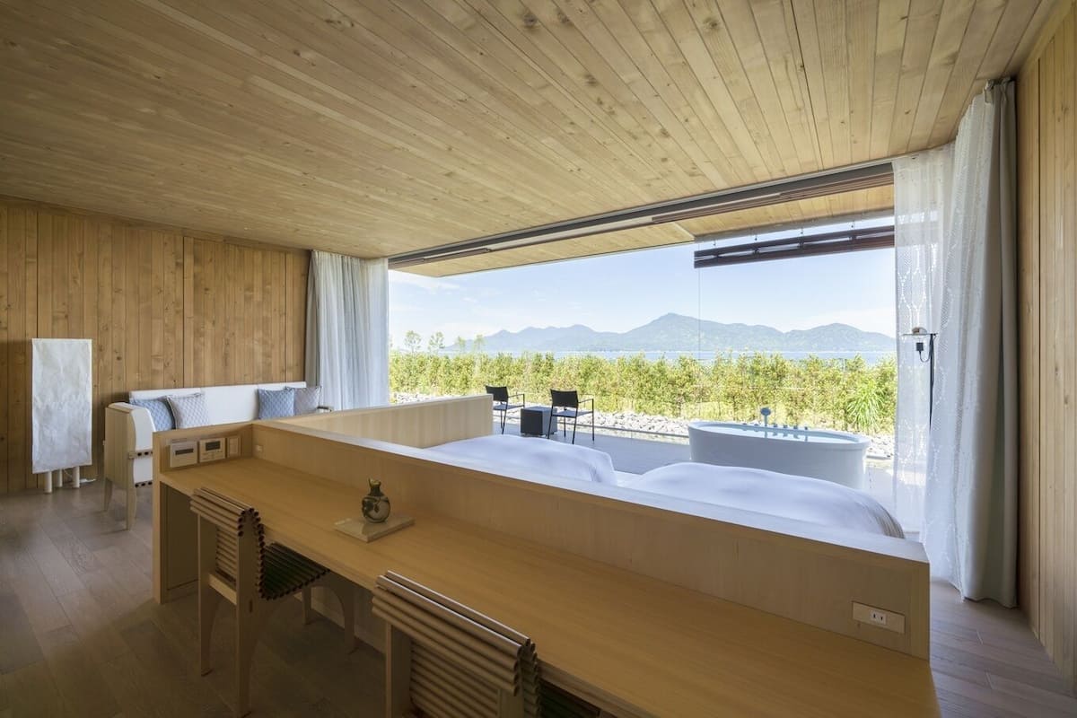 A modern room with a wooden ceiling, a large bed, a wooden desk, and a view of the mountains.