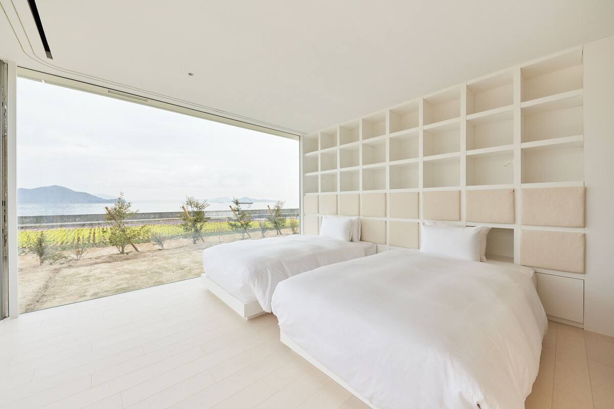 A bedroom with two beds, a large window, and a view of a landscape.