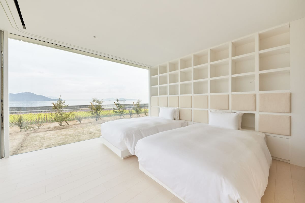 A bedroom with two beds, a large window, and a view of a landscape.