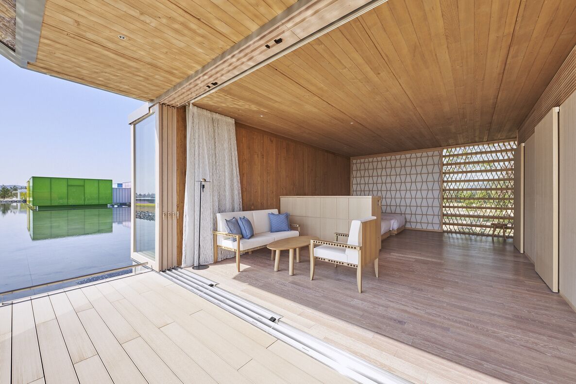 Un intérieur moderne avec un plafond en bois, un canapé, un fauteuil et une porte en verre donnant sur une piscine.