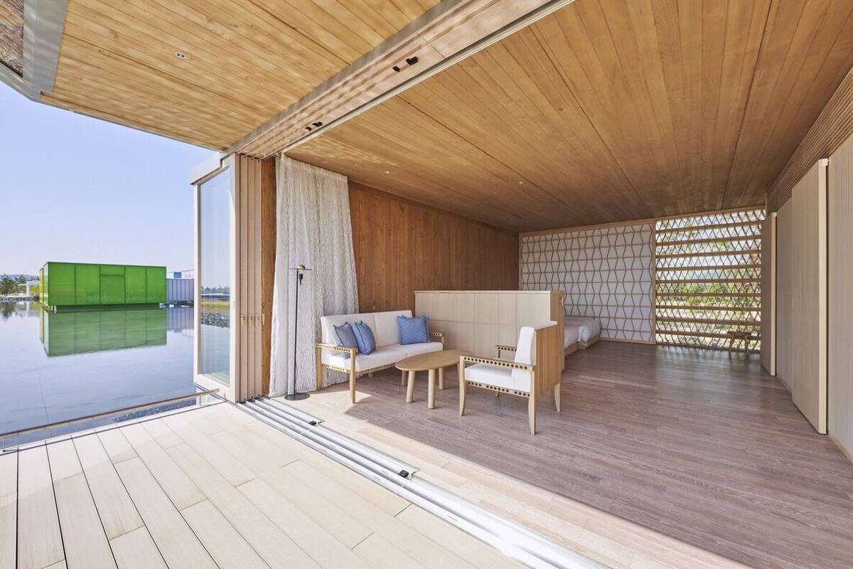 A modern interior with a wooden ceiling, a sofa, a chair, and a glass door leading to a pool.