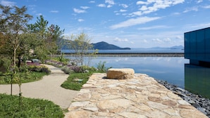 A stone pathway leading to a modern building with a view of a calm lake and mountains in the distance. - Simose Art Garden Villa (Otake)