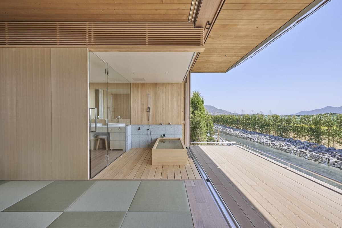 A modern interior with a wooden floor, a glass-enclosed bathroom, and a view of a vineyard.