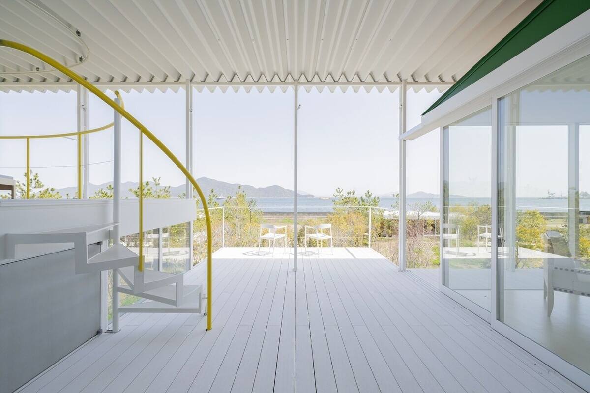A spacious balcony with a view of the sea and mountains, white railings, and a yellow spiral staircase.