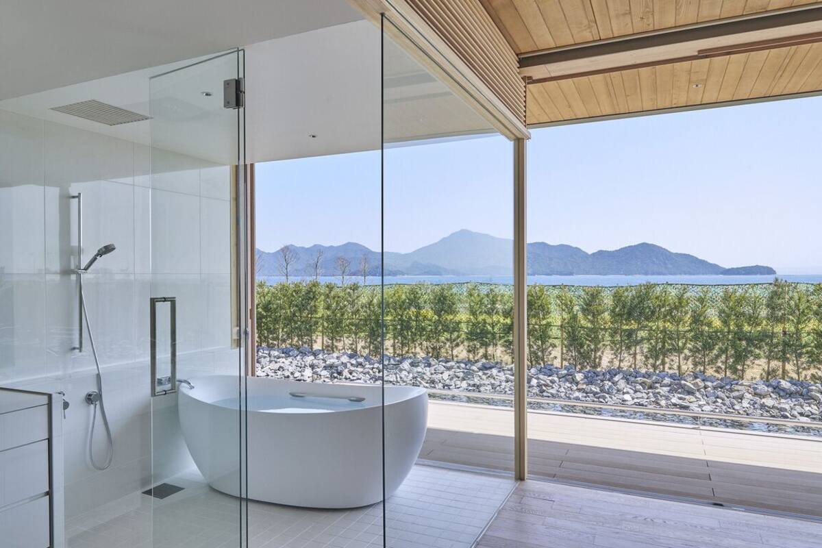A modern bathroom with a glass-enclosed shower, a freestanding bathtub, and a view of a mountainous landscape.