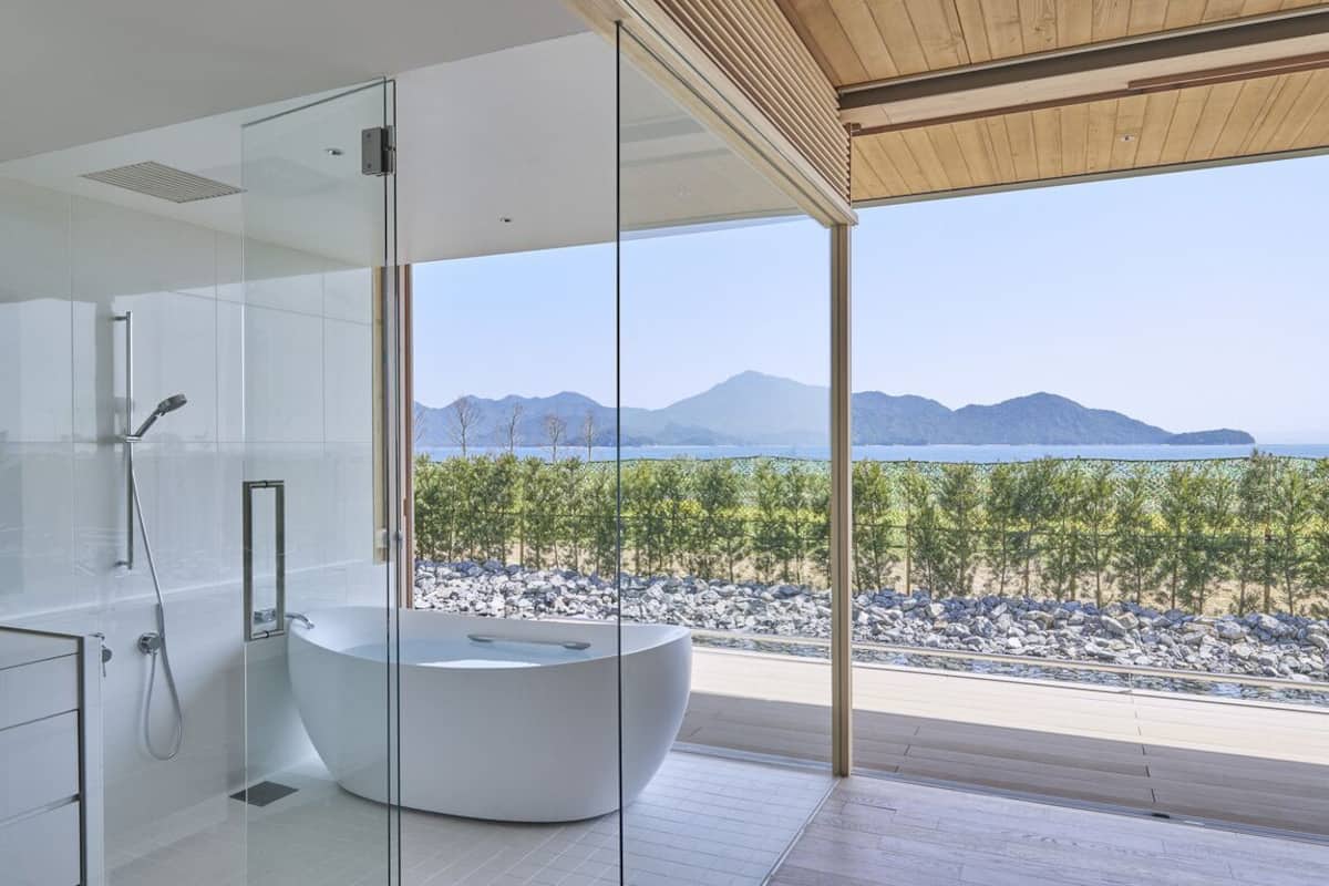 A modern bathroom with a glass-enclosed shower, a freestanding bathtub, and a view of a mountainous landscape.