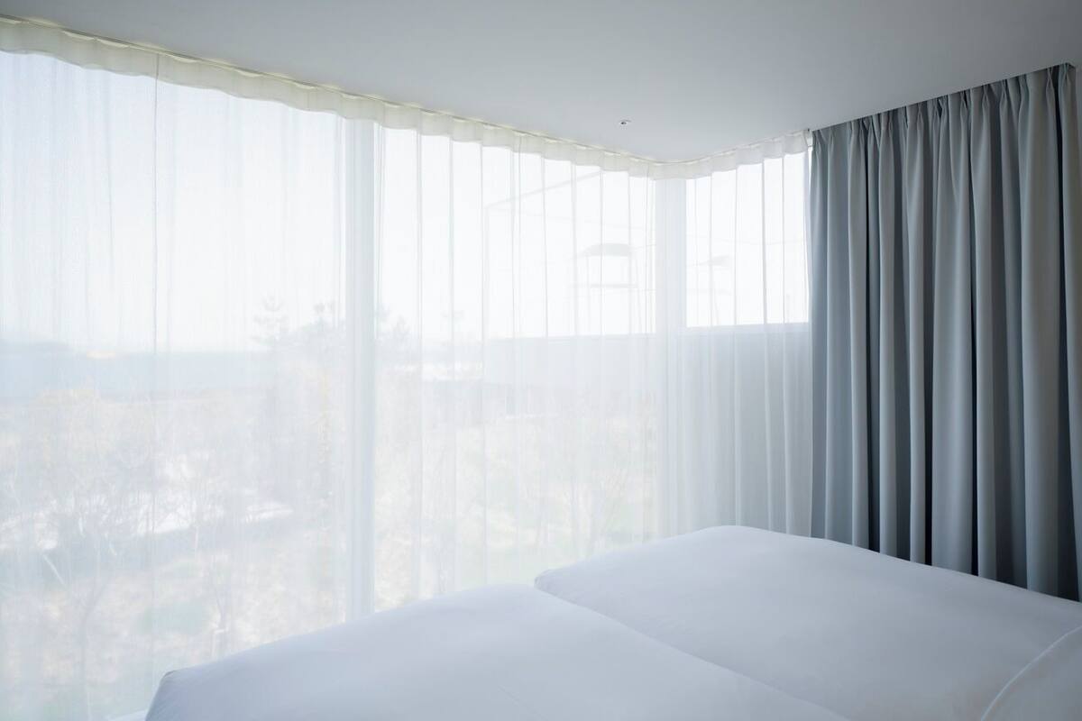 A hotel room with a large bed, sheer curtains, and a view of the city.